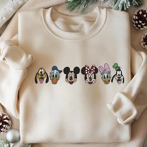 Puede incluir: Sudadera color crema con caras bordadas de personajes de dibujos animados: Pluto, Pato Donald, Mickey Mouse, Minnie Mouse, Daisy Duck y Goofy. La sudadera tiene cuello redondo y mangas largas, ideal para uso casual.