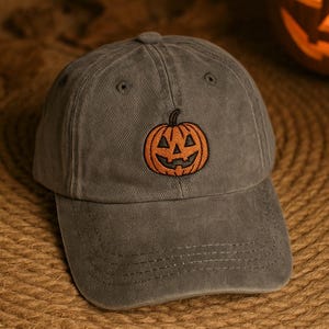 Puede incluir: Gorra de béisbol gris con un diseño bordado de calabaza naranja. La gorra tiene una visera curva y una construcción clásica de seis paneles. Perfecto para Halloween o el otoño.