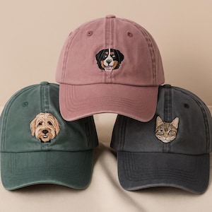 Op de afbeelding: Drie baseballpetten in stoffig roze, teal en antracietgrijs. Elke pet heeft een geborduurd dierengezicht: een hond, een kat en een andere hond. De petten hebben een klassiek, ongestructureerd ontwerp.