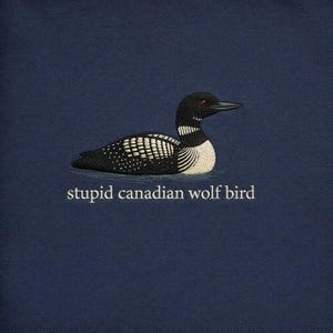 May include: A navy blue graphic featuring a detailed illustration of a loon with black, white, and red accents. The text "stupid canadian wolf bird" is printed below the bird.