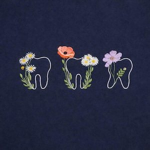 Könnte beinhalten: Stickdesign auf marineblauem Hintergrund mit drei Zahnkonturen, die jeweils mit bunten Blumen verziert sind. Die Blumen umfassen Gänseblümchen, eine Mohnblume und eine lila Blume mit grünen Stielen und Blättern.