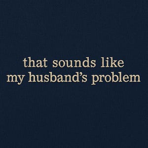 May include: Navy blue sweatshirt with the embroidered text "that sounds like my husband's problem" in a cream-colored thread. The text is centered on the front of the garment.