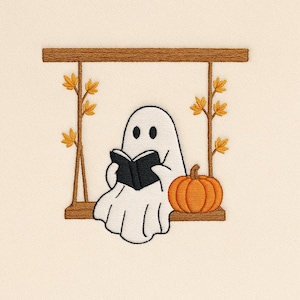 Puede incluir: Diseño bordado de un fantasma blanco leyendo un libro negro en un columpio de madera. Una calabaza naranja está junto al fantasma. El columpio está decorado con ramas marrones y hojas amarillas.