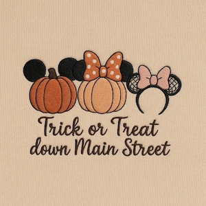 Puede incluir: Diseño bordado con tres calabazas con orejas de Mickey Mouse y un lazo de Minnie Mouse. Las calabazas son naranjas y beige, con un lazo blanco y negro. El texto "Trick or Treat down Main Street" está debajo.