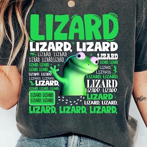 May include: Dark gray t-shirt with the word "LIZARD" in large green letters. The shirt features a cartoon lizard graphic and the word "LIZARD" repeated in various sizes and arrangements. The shirt is a comfortable, casual style.