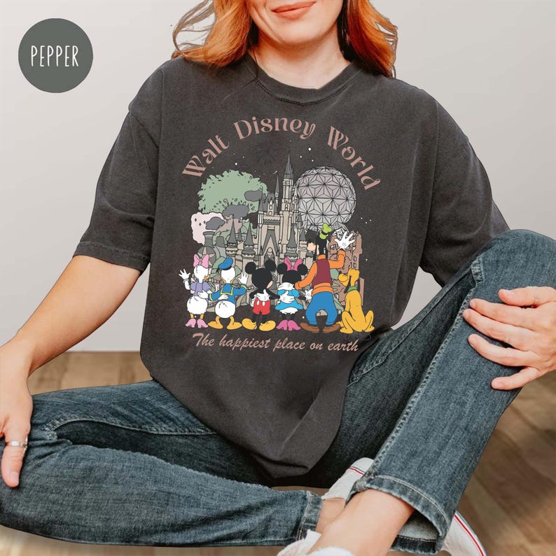 May include: Dark gray t-shirt featuring a Walt Disney World graphic. The design includes the park's logo, iconic characters like Mickey Mouse, and the phrase "The happiest place on earth."