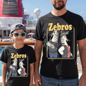 May include: Black t-shirts with the word "Zebros" in yellow, featuring a cartoon zebra design. The shirts are worn by a person and a child. The background includes a cruise ship and a pool.