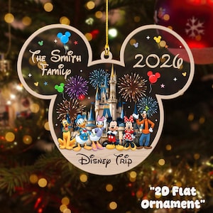 May include: A flat, Mickey Mouse-shaped Christmas ornament featuring a castle, fireworks, and cartoon characters including Pluto, Donald, Daisy, Mickey, Minnie, and Goofy. The text reads The Smith Family, 2026, and Disney Trip. It hangs by a gold cord.