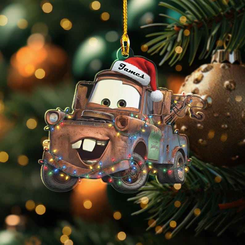 May include: A brown tow truck Christmas ornament with a Santa hat and the name "James" printed on it. The ornament is decorated with colourful string lights and is hanging from a gold string. A festive holiday decoration.