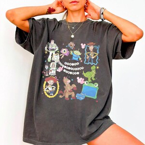 May include: A charcoal gray short-sleeve t-shirt featuring a graphic print of various Toy Story characters including Woody, Buzz Lightyear, Jessie, and Rex. The text "YOU'VE GOT A FRIEND IN ME" is printed in the center surrounded by small star and icon accents.