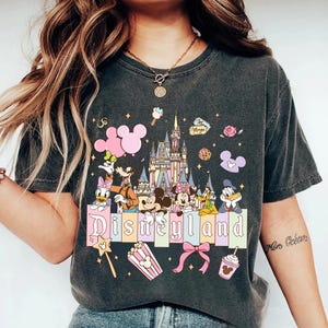Puede incluir: Camiseta gris oscuro con un dise&ntilde;o colorido de Disneyland. El dise&ntilde;o incluye a Mickey y Minnie Mouse, el Pato Donald, Goofy y Daisy, un castillo, globos y la palabra "Disneyland".