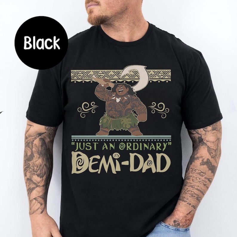 May include: Black t-shirt featuring a cartoon illustration of a character holding a hook. The text reads "JUST AN ORDINARY DEMI-DAD" in a stylized font. The design includes decorative elements.