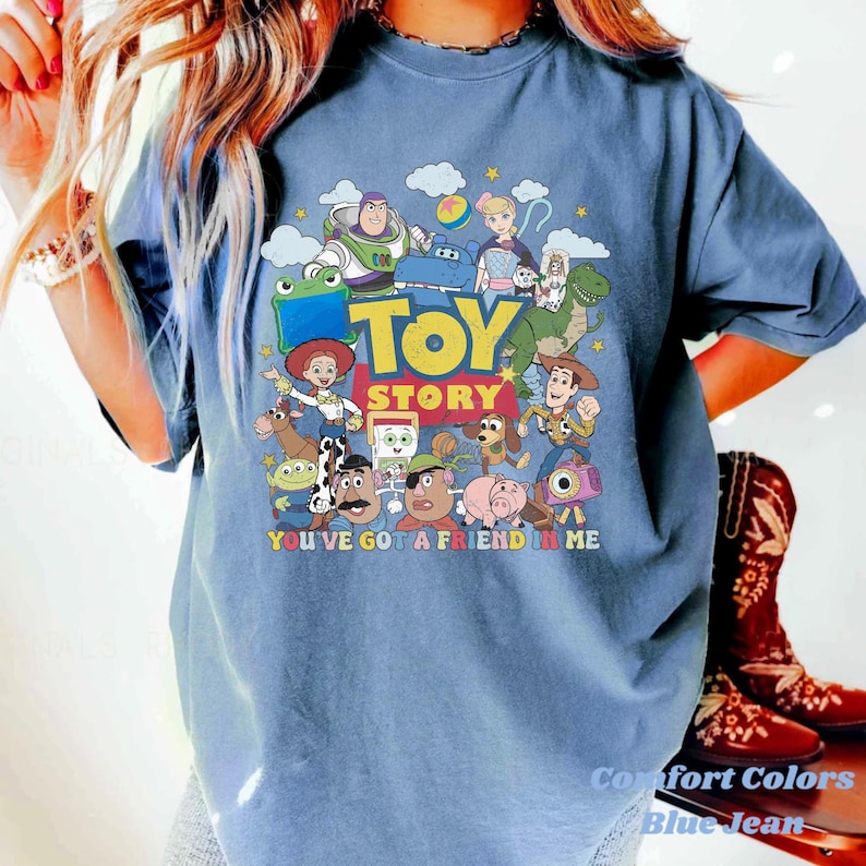 Puede incluir: Una camiseta azul de manga corta con un estampado gr&aacute;fico colorido de varios personajes de Toy Story, incluyendo a Woody, Buzz Lightyear y Jessie. El texto "TOY STORY" y "YOU'VE GOT A FRIEND IN ME" est&aacute; impreso en una fuente negrita multicolor.