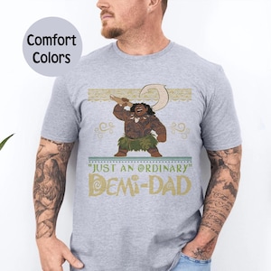 May include: Gray Comfort Colors t-shirt featuring a cartoon character with a hook, and the text "JUST AN ORDINARY DEMI-DAD" in gold and teal. The character is brown with a green grass skirt.