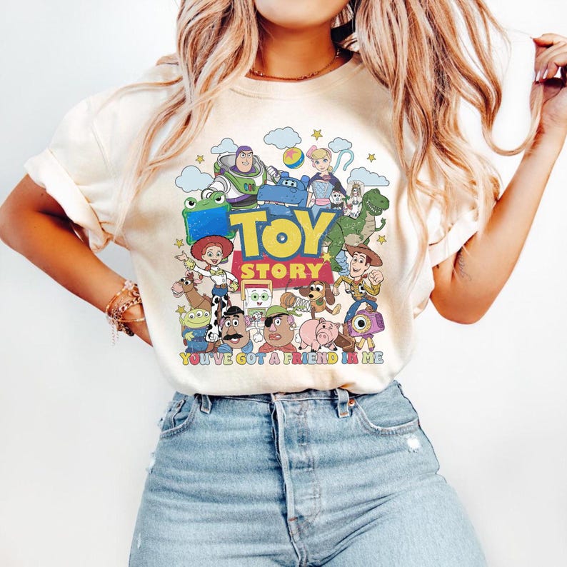 Puede incluir: Una camiseta de color crema con un estampado gr&aacute;fico colorido de los personajes de Toy Story, incluyendo a Woody, Buzz Lightyear, Jessie y Rex. El dise&ntilde;o incluye el texto TOY STORY y YOU'VE GOT A FRIEND IN ME en letras negritas multicolor.