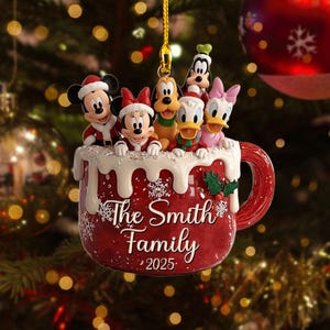 May include: A festive red mug-shaped Christmas ornament featuring Disney characters Mickey, Minnie, Pluto, Donald, Daisy, and Goofy. The mug is decorated with snowflakes and the text "The Smith Family 2025."