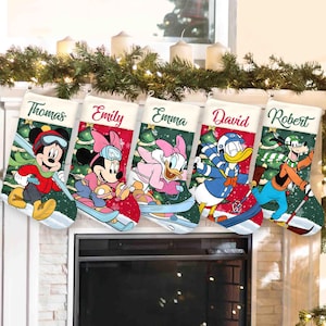 May include: Five personalized Christmas stockings featuring Disney characters skiing on a snowy background. Each stocking displays a name at the top: Thomas, Emily, Emma, David, and Robert. The characters include Mickey, Minnie, Daisy, Donald, and Goofy.