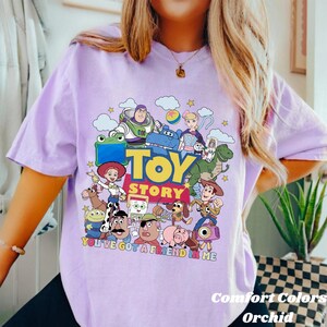 Puede incluir: Una camiseta de color morado claro con un estampado gr&aacute;fico colorido de los personajes de Toy Story, incluyendo a Woody, Buzz Lightyear, Jessie y Rex. El dise&ntilde;o incluye el texto "TOY STORY" y "YOU'VE GOT A FRIEND IN ME" en letras llamativas.