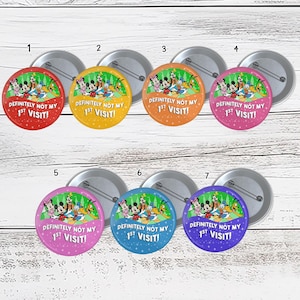 May include: Seven round pinback buttons with cartoon characters and the text "DEFINITELY NOT MY 1ST VISIT!" in various colors: red, yellow, orange, pink, purple, blue, and indigo. Each button has a silver pin backing.