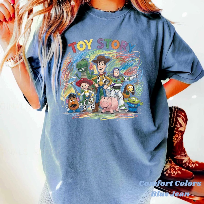 Peut inclure: T-shirt bleu jean avec l'inscription "TOY STORY" en lettres color&eacute;es au-dessus d'un dessin des personnages du film d'animation. Le t-shirt est de la marque Comfort Colors.
