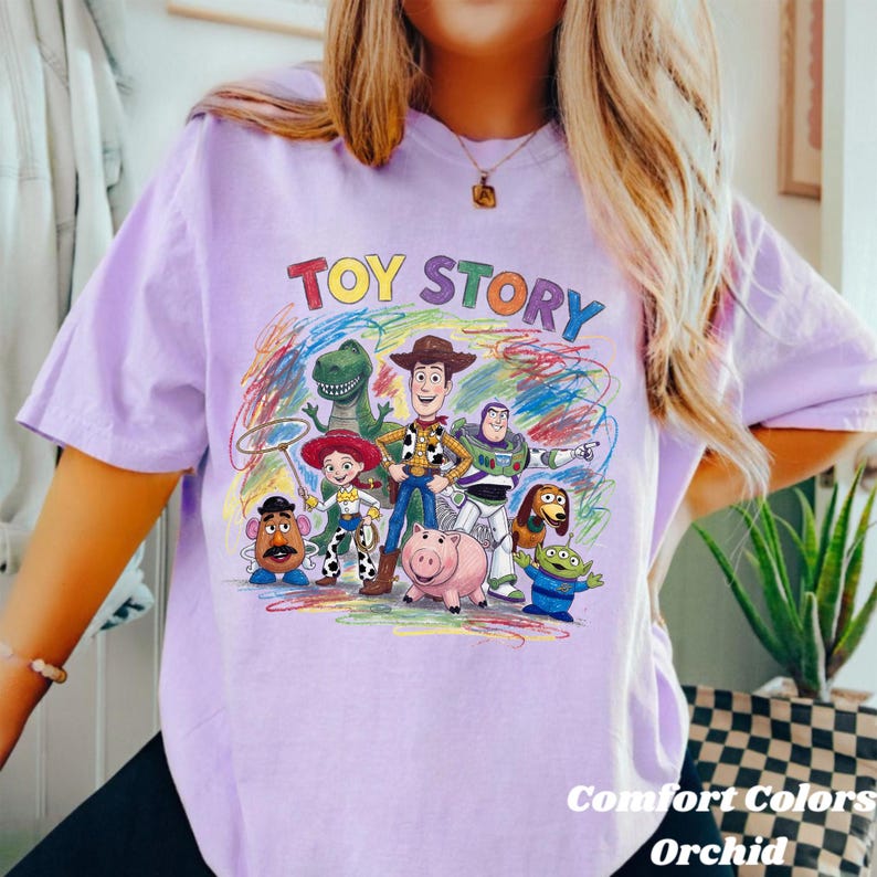 Peut inclure: T-shirt lilas avec l'inscription multicolore "TOY STORY" au-dessus d'un dessin des personnages du film d'animation. Le t-shirt porte &eacute;galement l'inscription "Comfort Colors Orchid" en bas &agrave; droite.