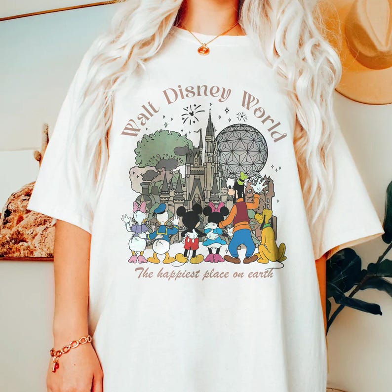 May include: Cream-colored t-shirt featuring a colorful graphic of Disney characters and landmarks, including Mickey and Minnie Mouse, Goofy, and Cinderella's castle. The text "Walt Disney World" and "The happiest place on earth" are printed above and below the illustration.