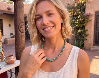 May include: A necklace featuring small, irregular, polished turquoise stones in shades of blue and green, strung together on a cord. The necklace sits at the base of the neck, showcasing the natural variations in the color and shape of the stones.