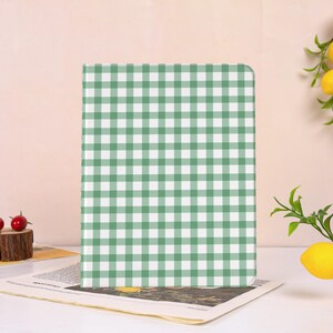 Op de afbeelding: Een rechthoekig object met een groen en wit ruitpatroon. Het object staat rechtop op een krant. De achtergrond is lichtroze.