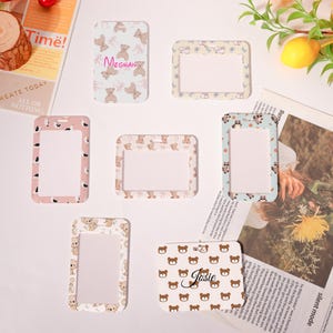 May include: Several rectangular ID badge holders with different patterns. Some have teddy bear designs, others have solid colours or floral patterns. One holder displays the name "Meghan," and another says "Josie."