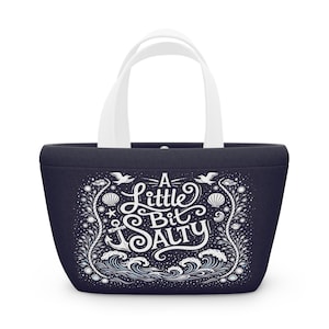 以下が含まれることがあります： 白の持ち手が付いた濃いネイビーのトートバッグ。「A Little Bit Salty」の文字が白で書かれた航海をテーマにしたデザイン。デザインには、錨、波、貝殻、鳥が含まれています。
