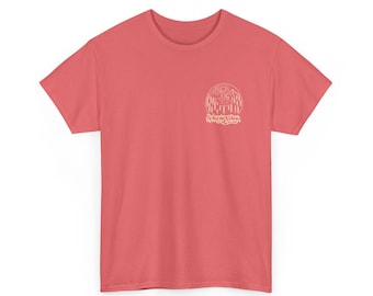 May include: A coral-colored t-shirt with a crew neck and short sleeves. A white circular graphic on the upper left chest features a mountain scene and the text "Wander Often, Wonder Always."