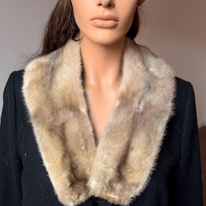 May include: A vintage ensemble featuring a light brown fur hat and a matching fur collar. The hat has a rounded shape with a decorative knot. The collar is worn over a black garment, creating a classic, elegant look.