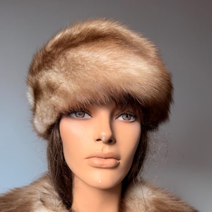 Puede incluir: Un maniquí con un sombrero de piel marrón y un abrigo de piel a juego. La piel tiene un aspecto suave y texturizado con diferentes tonos de marrón y beige. El sombrero es redondo y el abrigo cae sobre los hombros.