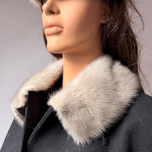 May include: A black coat with a light gray fur collar and matching fur hat. The coat has a classic design, and the fur appears soft and luxurious. The hat sits atop the head, completing the elegant ensemble. The overall look is sophisticated and warm.