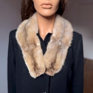 May include: A black coat with a light brown fur collar. The coat has a classic design with a button closure. The fur collar adds a touch of luxury and warmth to the garment. The coat is displayed on a mannequin.