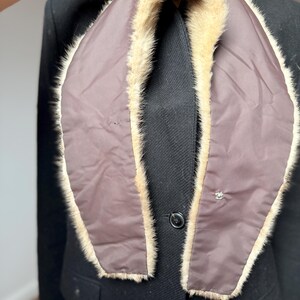 May include: A brown and beige fur collar with a dark brown lining. The collar is draped over a black coat, showcasing the contrast between the textures and colors. A small decorative button is visible on the coat.