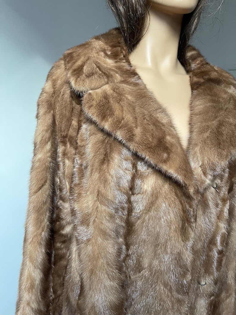Pu&ograve; includere: Un cappotto di pelliccia marrone con colletto classico e chiusura con bottoni. Il cappotto ha un aspetto morbido e strutturato e un colore marrone medio. Il cappotto &egrave; esposto su un manichino.