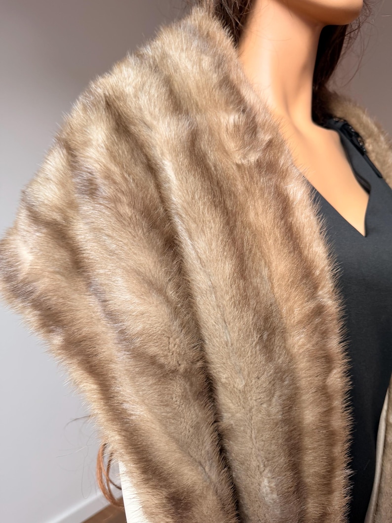 Pode incluir: Uma luxuosa estola de pele castanho-clara com um aspeto macio e texturizado. A estola est&aacute; drapeada sobre uma pe&ccedil;a de roupa preta, mostrando a sua cor rica e textura macia. A pele parece estar em excelentes condi&ccedil;&otilde;es, sugerindo alta qualidade.