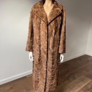 Pu&ograve; includere: Un cappotto lungo di pelliccia marrone con colletto classico e chiusura con bottoni. Il cappotto &egrave; esposto su un manichino, mettendo in risalto il suo design strutturato e fantasia. Il cappotto sembra essere vintage, con un'estetica lussuosa e calda.