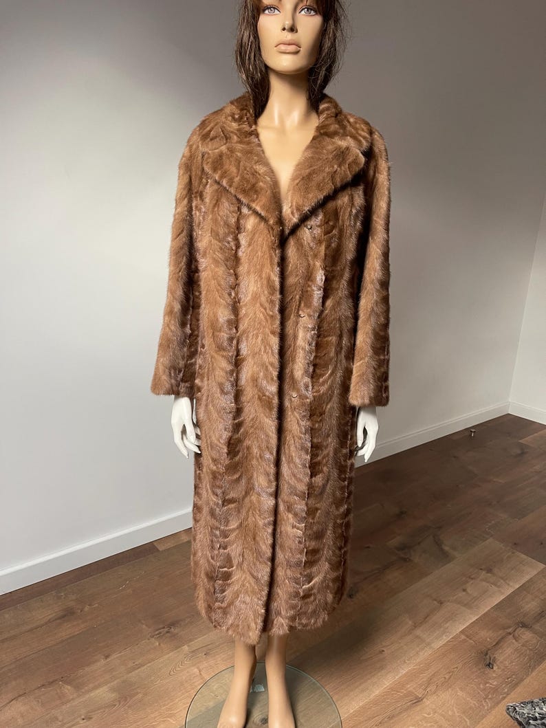 Pu&ograve; includere: Un cappotto lungo di pelliccia marrone con colletto classico e chiusura con bottoni. Il cappotto &egrave; esposto su un manichino, mettendo in risalto il suo design strutturato e fantasia. Il cappotto sembra essere vintage, con un'estetica lussuosa e calda.