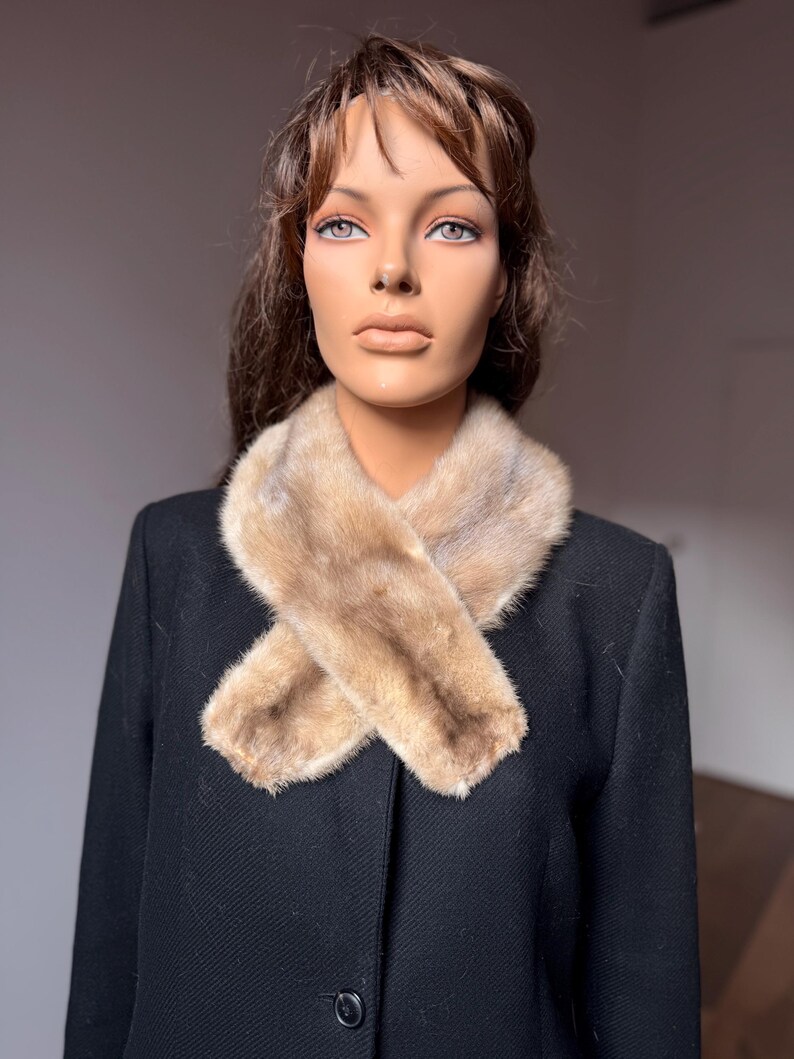 May include: A black coat with a light brown fur collar. The fur collar is crossed over the chest. The coat is buttoned up and has a classic design. The mannequin has brown hair and is looking forward.