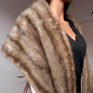 Pode incluir: Uma luxuosa estola de pele castanha com um padr&atilde;o listrado. A estola &eacute; drapeada sobre um vestido preto, mostrando sua textura e varia&ccedil;&otilde;es de cor. A pele parece macia e felpuda, adicionando um toque de eleg&acirc;ncia.