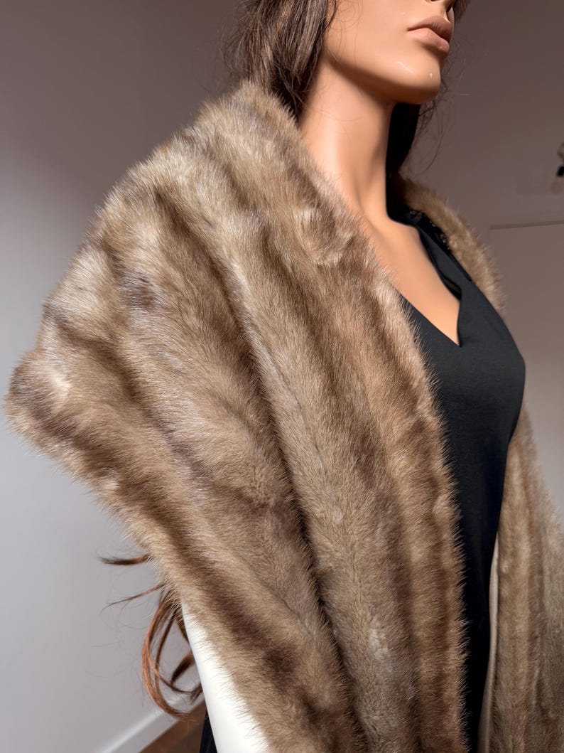Pode incluir: Uma luxuosa estola de pele castanha com um padr&atilde;o listrado. A estola &eacute; drapeada sobre um vestido preto, mostrando sua textura e varia&ccedil;&otilde;es de cor. A pele parece macia e felpuda, adicionando um toque de eleg&acirc;ncia.