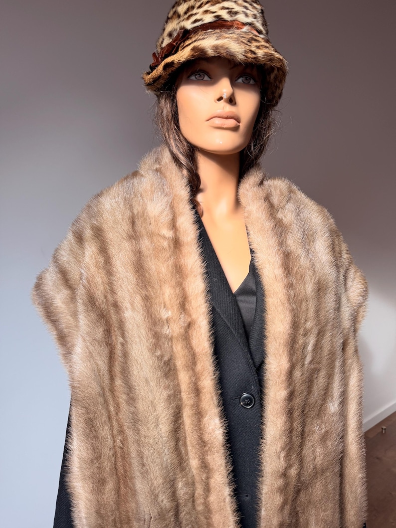 Pode incluir: Um manequim vestindo uma estola de pele vintage e um chap&eacute;u com estampa de leopardo. A estola de pele &eacute; marrom claro e cobre um blazer preto. O chap&eacute;u tem uma fita marrom e um padr&atilde;o de leopardo.