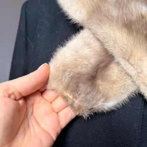 May include: Close-up of a vintage black coat with a light brown fur collar and cuffs. The fur has a soft, textured appearance. The coat's fabric is a dark, woven material.