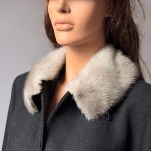 May include: A black coat with a light gray fur collar and matching fur hat. The coat has a classic design with a tailored fit. The fur collar and hat add a touch of luxury and warmth. The coat is displayed on a mannequin.