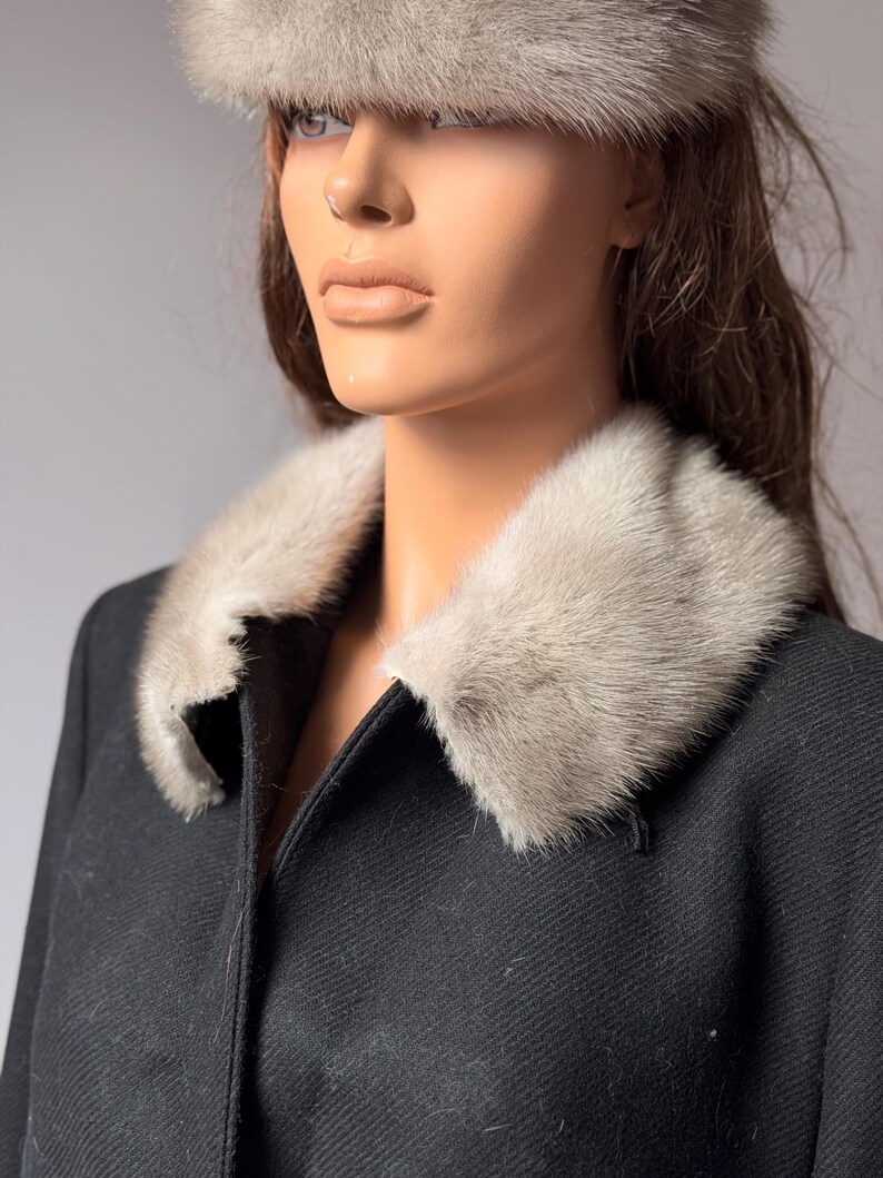 May include: A black coat with a light gray fur collar and matching fur hat. The coat has a classic design with a tailored fit. The fur collar and hat add a touch of luxury and warmth. The coat is displayed on a mannequin.