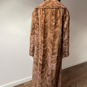 Pu&ograve; includere: Un cappotto di pelliccia marrone lungo fino a terra esposto su un manichino. Il cappotto ha un colletto a revers e maniche lunghe. La pelliccia &egrave; di un ricco e caldo colore marrone con un motivo strutturato. Il manichino &egrave; posizionato di spalle.