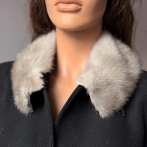 May include: A black coat with a light gray fur collar. The coat has a classic design with a notched collar and a tailored fit. The fur collar adds a touch of luxury and warmth to the garment. The coat is made of a textured fabric.