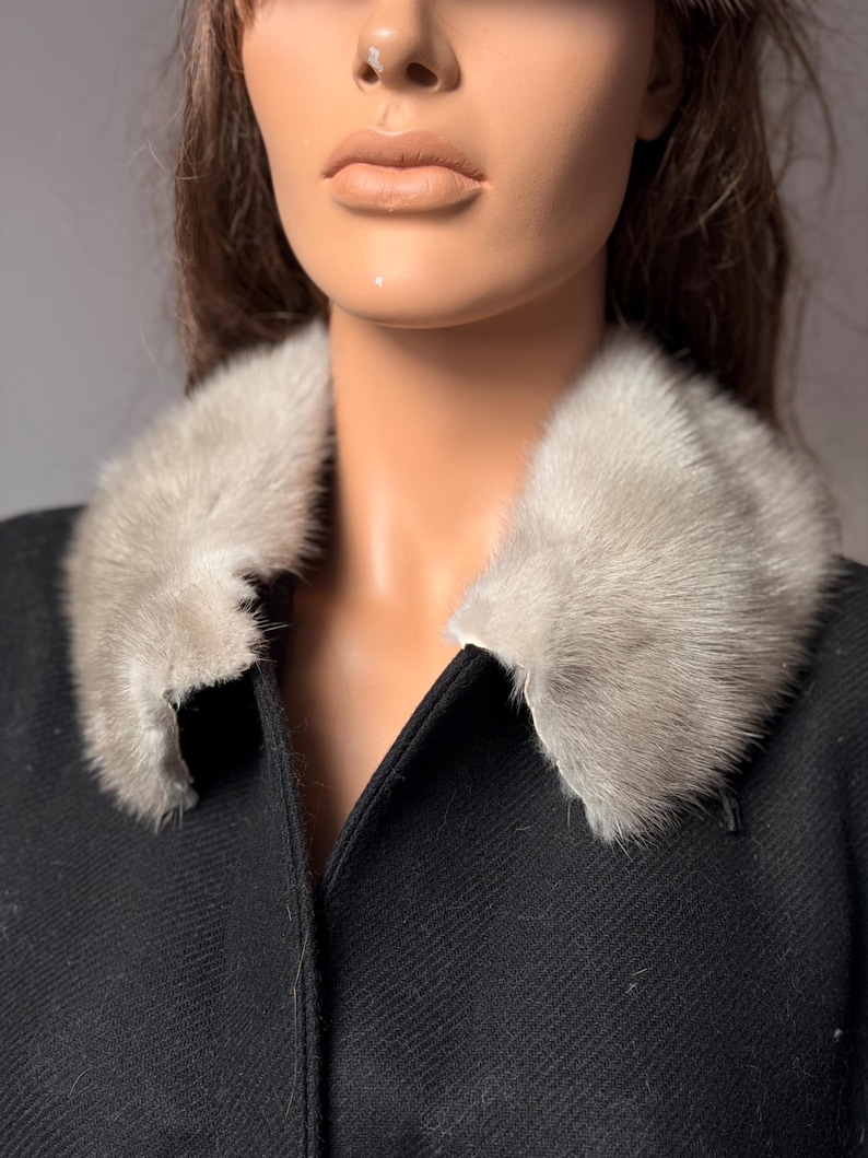 May include: A black coat with a light gray fur collar. The coat has a classic design with a notched collar and a tailored fit. The fur collar adds a touch of luxury and warmth to the garment. The coat is made of a textured fabric.